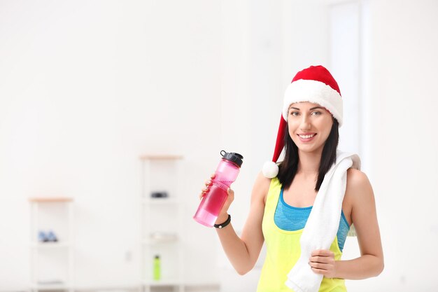 Hermosa mujer joven con sombrero de Santa Claus con botella de agua en el gimnasio