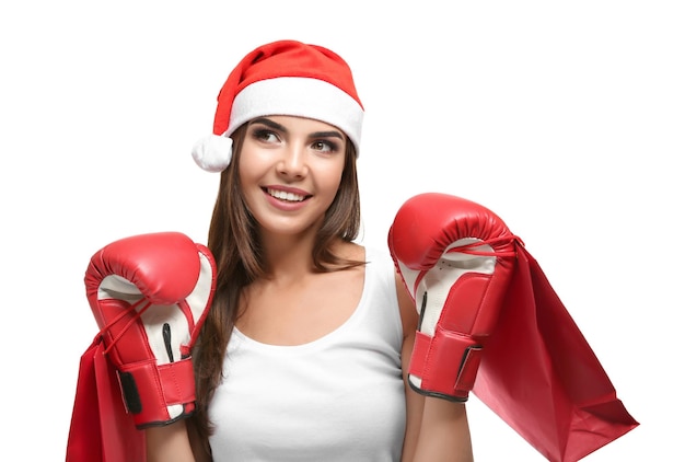 Hermosa mujer joven con sombrero de Santa Claus con guantes de boxeo y bolsas de compras sobre fondo blanco. Concepto del día de San Esteban