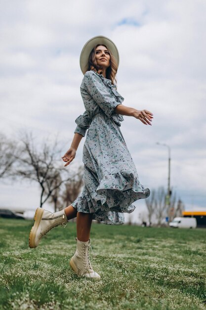 Hermosa mujer joven con un sombrero y un vestido azul está bailando en un campo de flores silvestres Primavera