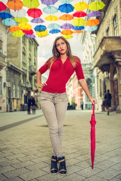 Hermosa mujer joven con sombrilla roja en la calle decorada con muchas sombrillas multicolores.