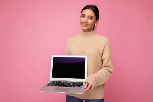 Hermosa mujer joven sonriente con cabello oscuro mirando a la cámara sosteniendo la computadora portátil con vacío