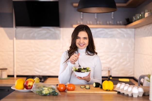 Hermosa mujer joven sonriente preparando alimentos saludables con muchas frutas y verduras en la cocina de casa.