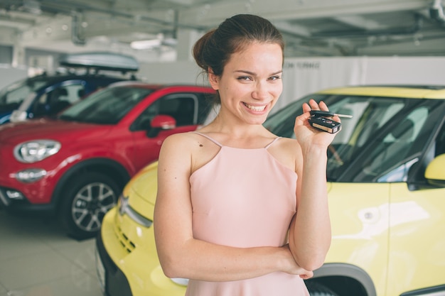 Foto hermosa mujer joven está sosteniendo una llave en el concesionario de automóviles. negocio de automóviles, venta de automóviles, - modelo femenino feliz en el salón del automóvil o salón.