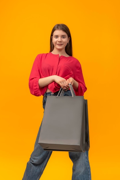 Hermosa mujer joven sostiene bolsas de compras de papel negro sobre fondo amarillo Espacio de copia Mockup Marco vertical