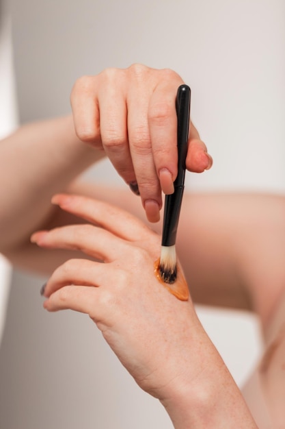 Hermosa mujer joven sostiene un pincel de maquillaje y aplica crema resaltadora en su mano closeup Belleza y maquillaje