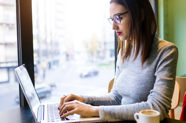 Foto hermosa mujer joven con su computadora portátil en la cafetería.