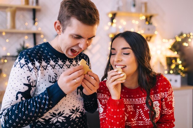 Hermosa mujer joven con su esposo en la cocina de Año Nuevo están preparando y probando galletas comidas tradicionales familiares comida casera saludable vacaciones de invierno