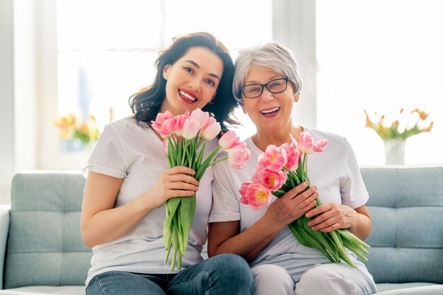 Hermosa mujer joven y su madre con flores tulipanes en manos en casa