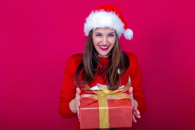 Hermosa mujer joven en suéter rojo y sombrero de Santa Claus ofreciendo un regalo con una gran sonrisa