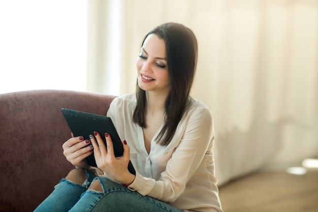 Hermosa mujer joven con tableta en casa en el sofá