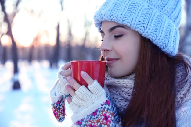 Hermosa mujer joven con una taza de café caliente al aire libre el día de invierno