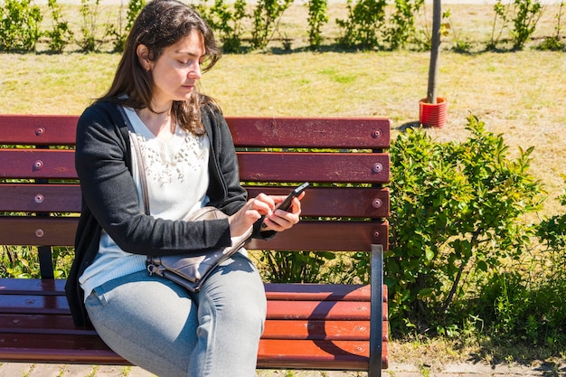 Hermosa mujer joven con un teléfono en un banco del parque en verano