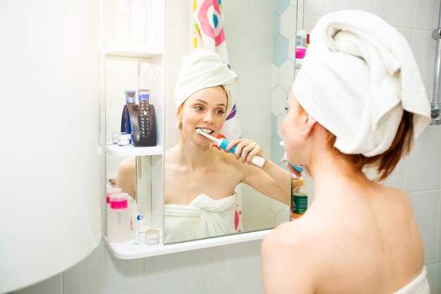 Foto hermosa mujer joven en una toalla en el baño se cepilla los dientes