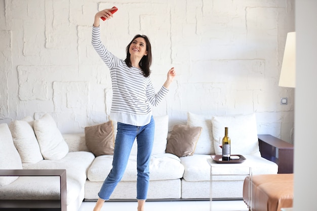 Hermosa mujer joven tomando selfie con smartphone en casa cerca del sofá.