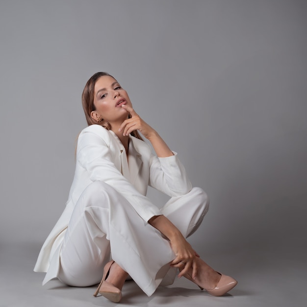 Hermosa mujer joven en un traje blanco de moda y zapatos de tacón beige