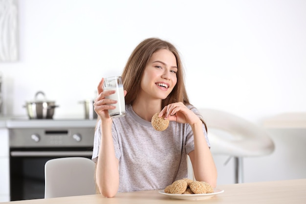 Hermosa mujer joven con vaso de leche y sabrosas galletas en casa