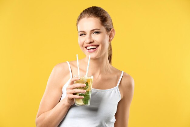 Hermosa mujer joven con vaso de limonada sobre fondo de color