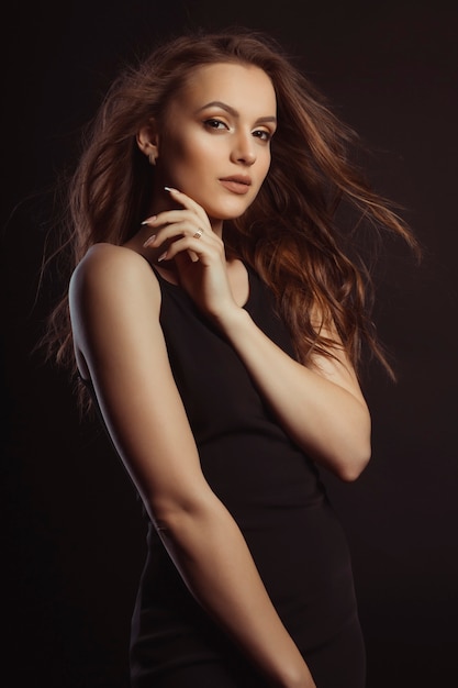 Hermosa mujer joven vestida de negro en el estudio. El viento sopla el cabello