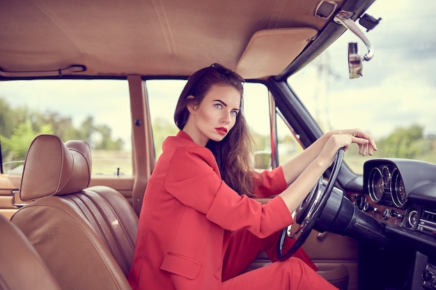 Hermosa mujer joven vestida con rojo costumesitting en coche retro