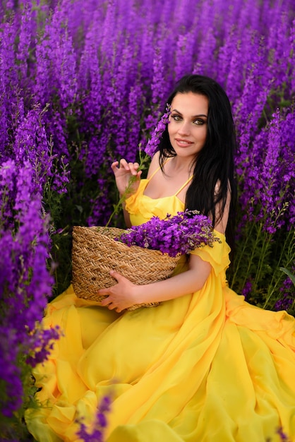 Hermosa mujer joven con un vestido amarillo se sienta en un campo de flores de color púrpura.