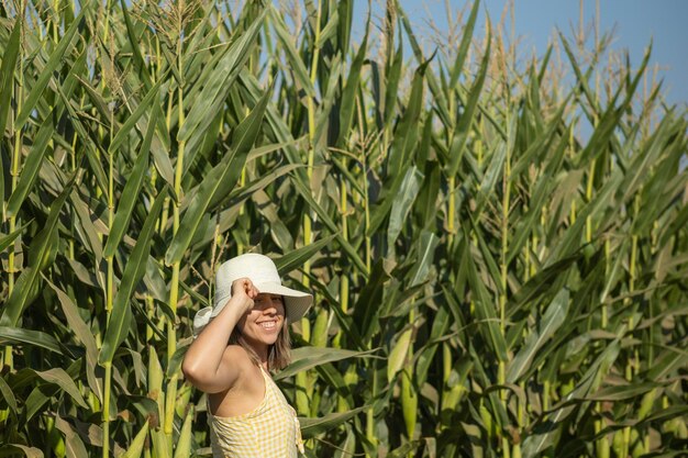 Foto hermosa mujer joven con un vestido amarillo y un sombrero de paja en un campo de maíz