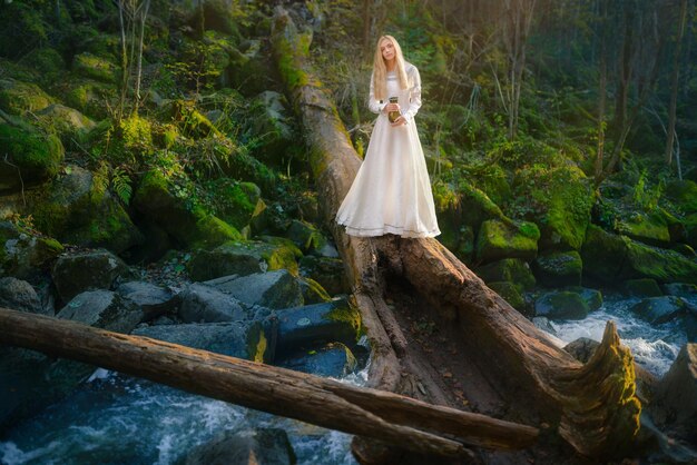 Hermosa mujer joven con un vestido blanco camina en medio de un bosque