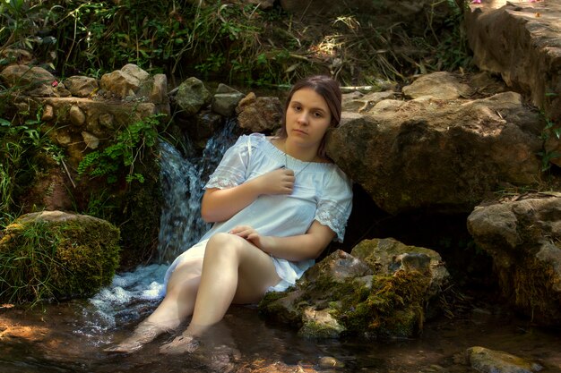 Hermosa mujer joven con vestido blanco junto a la corriente de agua.