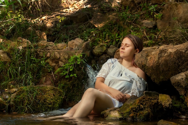 Hermosa mujer joven con vestido blanco junto a la corriente de agua.