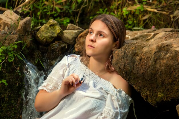 Hermosa mujer joven con vestido blanco junto a la corriente de agua.