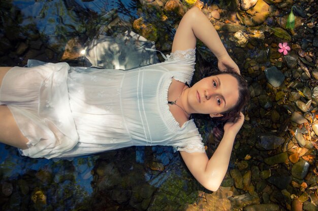 Hermosa mujer joven con vestido blanco junto a la corriente de agua.