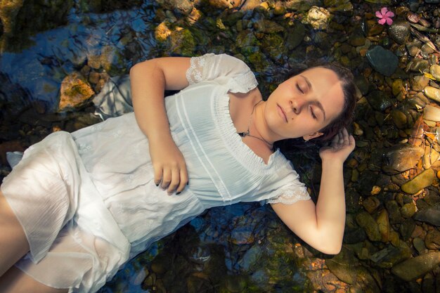 Hermosa mujer joven con vestido blanco junto a la corriente de agua.