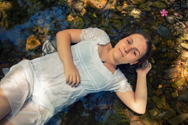 Hermosa mujer joven con vestido blanco junto a la corriente de agua.