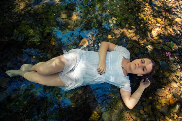 Hermosa mujer joven con vestido blanco junto a la corriente de agua.