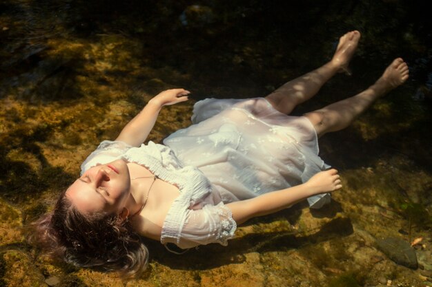 Hermosa mujer joven con vestido blanco junto a la corriente de agua.