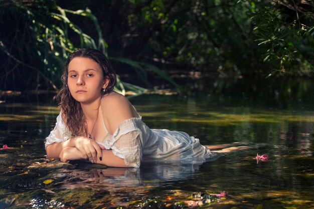 Hermosa mujer joven con vestido blanco junto a la corriente de agua.