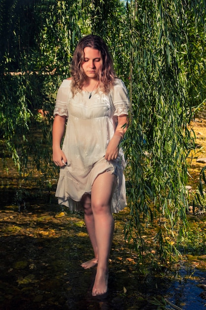 Hermosa mujer joven con vestido blanco junto a la corriente de agua.