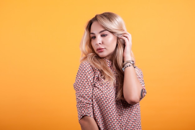 Hermosa mujer joven en vestido corto jugando con su cabello en estudio sobre fondo amarillo