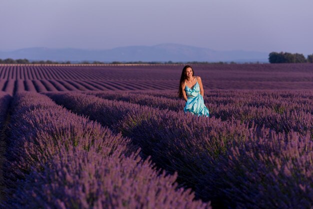 hermosa mujer joven en vestido cyand relajándose y divirtiéndose en el viento en el campo de flores de lavanda púrpura