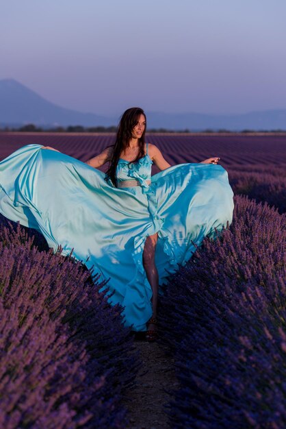 Foto hermosa mujer joven en vestido cyand relajándose y divirtiéndose en el viento en el campo de flores de lavanda púrpura