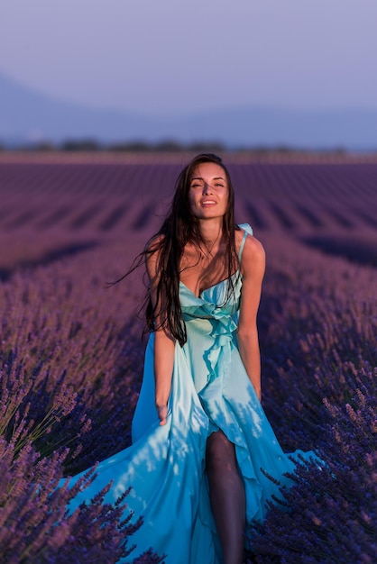 hermosa mujer joven en vestido cyand relajándose y divirtiéndose en el viento en el campo de flores de lavanda púrpura