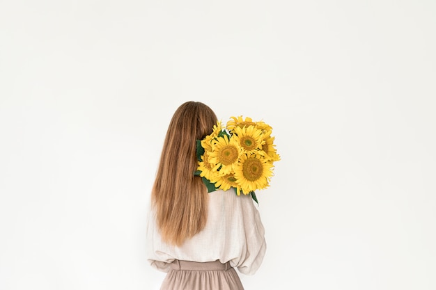 Hermosa mujer joven en vestido de lino con ramo de girasoles en blanco