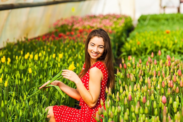 Hermosa mujer joven en vestido de lunares sentada en un campo de tulipanes al atardecer.