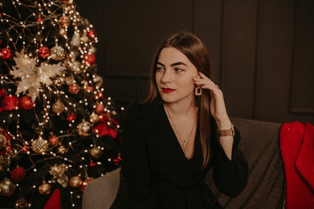Hermosa mujer joven con un vestido negro cerca de un árbol de Navidad en guirnaldas