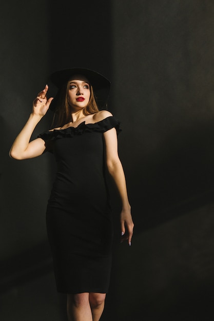 Hermosa mujer joven en vestido negro y sombrero sobre fondo negro