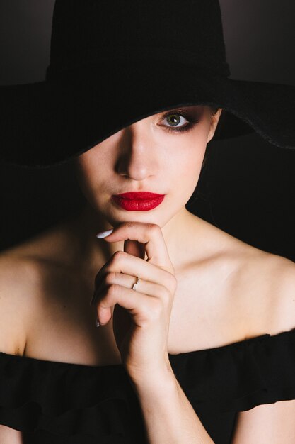 Hermosa mujer joven en vestido negro y sombrero sobre fondo negro