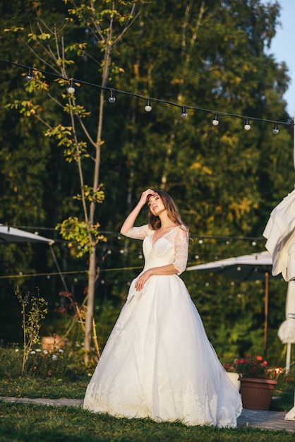 Hermosa mujer joven en un vestido de novia blanco y botas negras al atardecer.