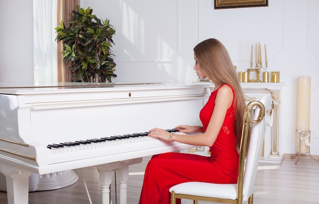 Foto hermosa mujer joven en un vestido rojo tocando el piano