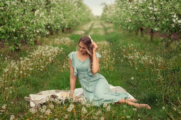 Hermosa mujer joven con un vestido romántico en un picnic en primavera en un jardín floreciente