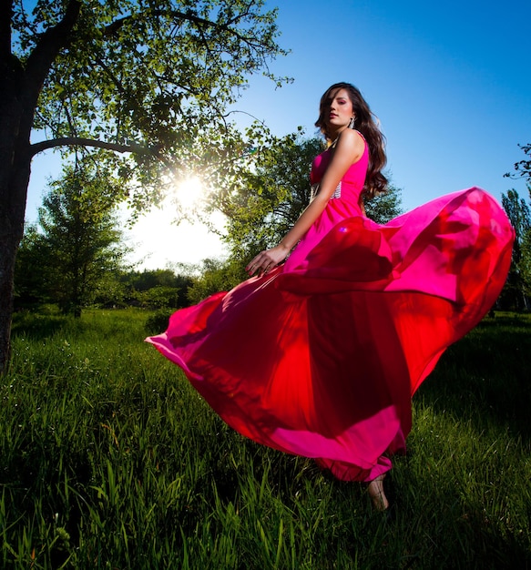 Hermosa mujer joven en un vestido rosa de pie sobre la hierba