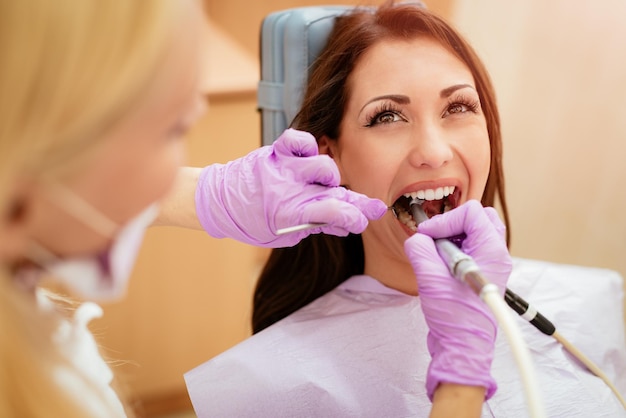 Hermosa mujer joven en visita a la oficina del dentista. Ella está sentada en una silla y el dentista le repara los dientes. Enfoque selectivo.